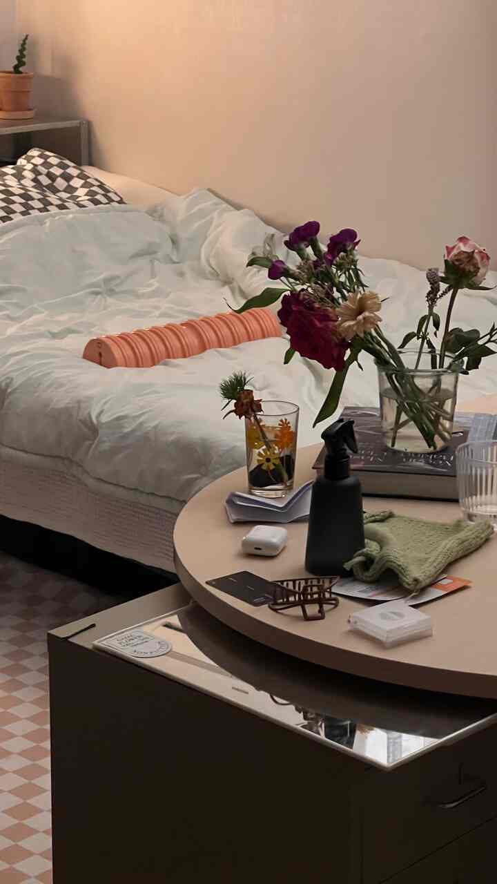 ホワイトとベージュの色調の寝室、白い寝具とベージュの丸テーブルに花瓶や様々な小物が配置された雰囲気のある空間