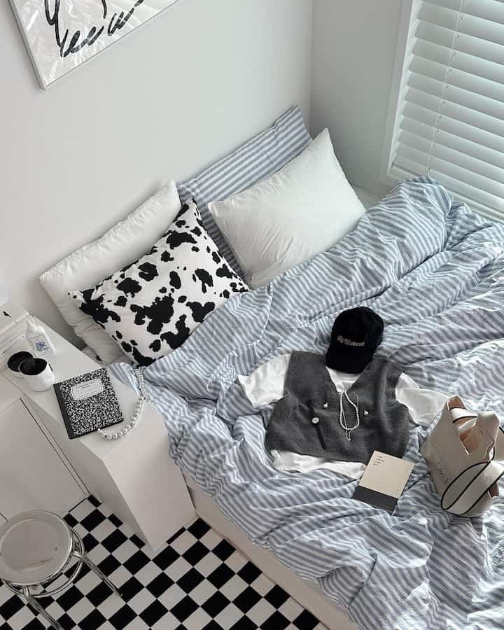 Bright bedroom in white and pastel blue tones featuring striped bedding and a black-and-white checkerboard floor