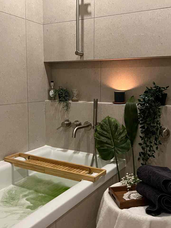 ナチュラルな色調のタイル壁と白い浴槽、木製トレイと造花が配置された居心地の良いバスルーム