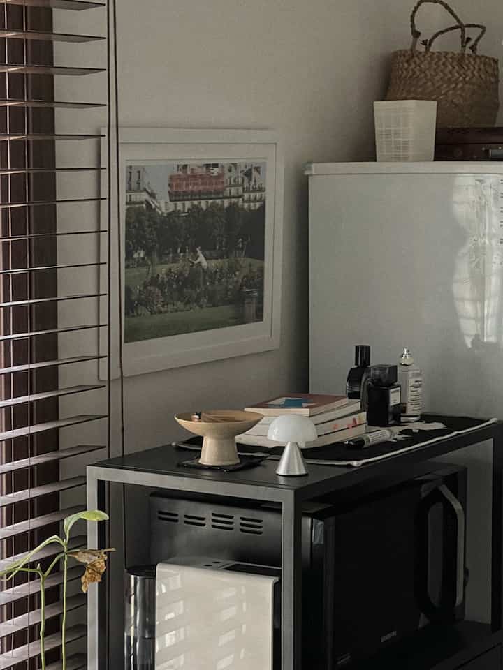 Charcoal and white toned kitchen featuring black metal shelves, refrigerator, and microwave with a modern, clean atmosphere