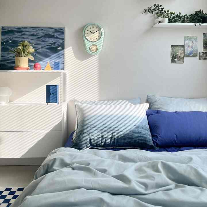Blue and white-toned bedroom featuring blue duvet cover and pillows, mint green wall clock and shelves on the wall creating a clean atmosphere