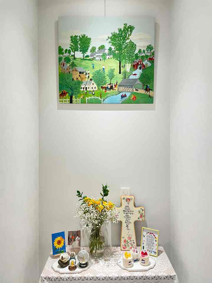 White-walled entrance space with lace tablecloth, featuring natural flower vase and framed painting, creating a cozy atmosphere