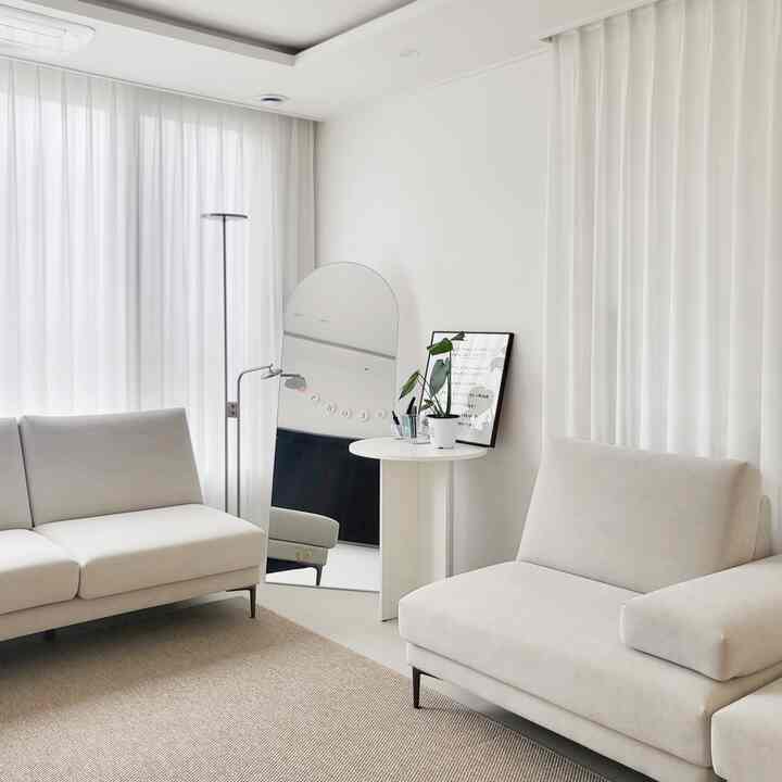 White and beige toned living room with two sofas and an arched full-length mirror, featuring a minimal and clean atmosphere