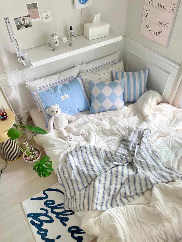 白と青のトーンの6畳の寝室、クッションと枕が配置された雰囲気のある寝具空間