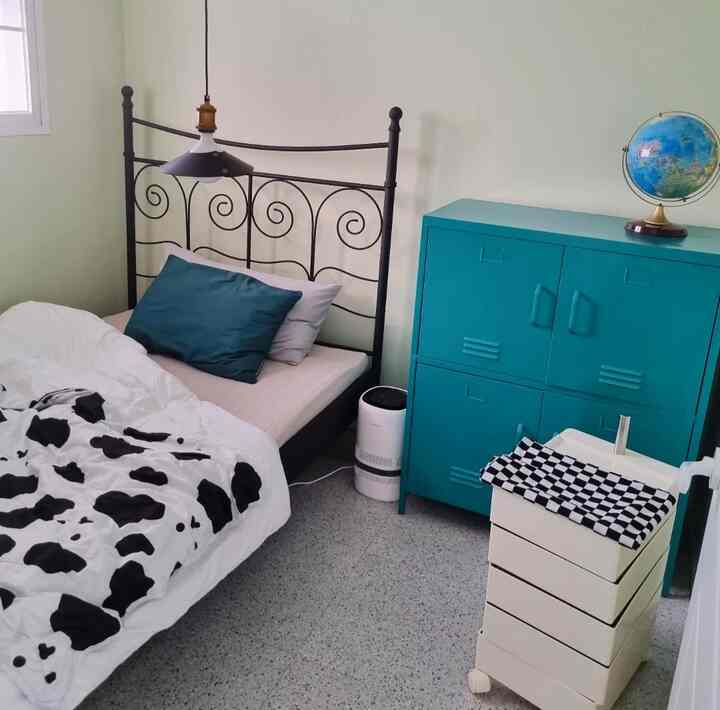 Small bedroom with white walls and floor accented by navy, featuring iron bed and turquoise cabinet in a modern setting