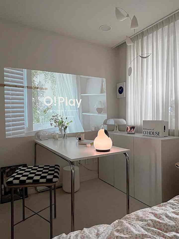 Small white-toned bedroom space featuring a desk, stool, table lamps, and sheer white curtains with a minimalistic atmosphere