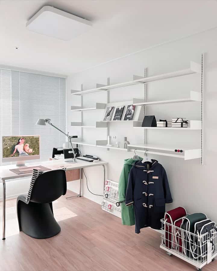白と木目調の調和が取れた書斎、デスクとコンピュータ、壁の棚、子供のコートと収納バスケットが配置された整然としたインテリア