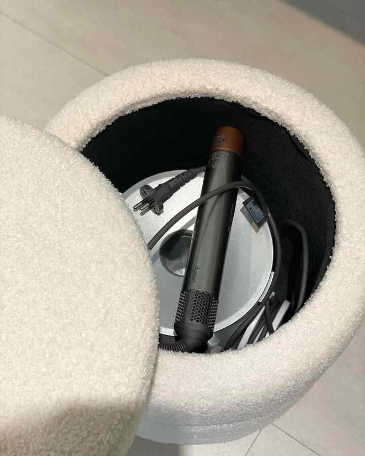 Minimal space featuring a white boucle fabric round storage stool neatly holding a Dyson Airwrap inside