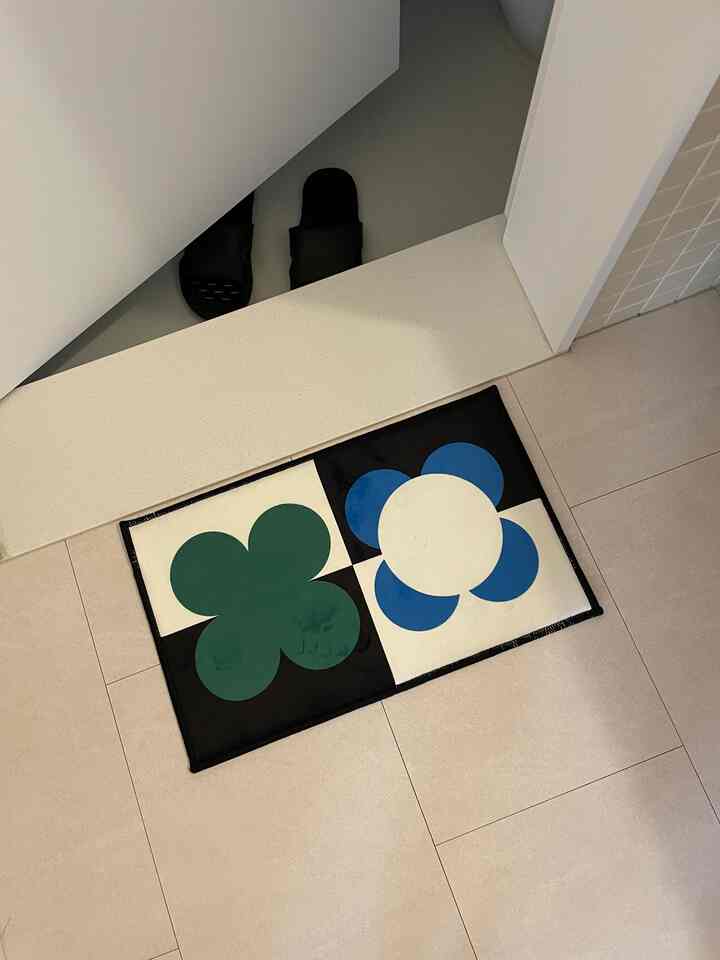 緑と青の花柄が施されたミニウェルカムマットがバスルームの入口に置かれたシンプルな玄関スペース