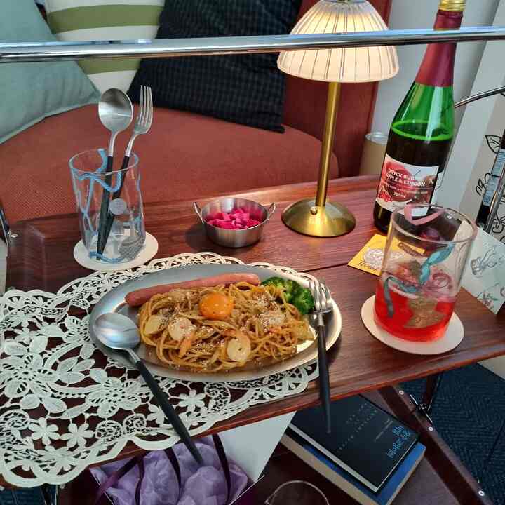 ブラウン木目調のキッチンワゴンの上に食事とグラスが置かれ、背景に赤いソファが見える温かみのあるダイニングスペース