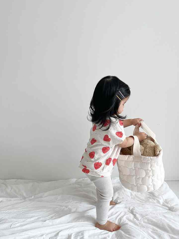 白を基調としたナチュラルな子供部屋、幼児が白い収納バスケットにおもちゃを入れる穏やかな雰囲気のインテリア