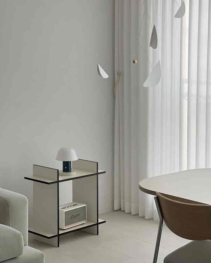 ホワイトとナチュラルウッドトーンが調和したリビング、ミニマルな棚とモビール、木製の椅子が配置されたシンプルな空間