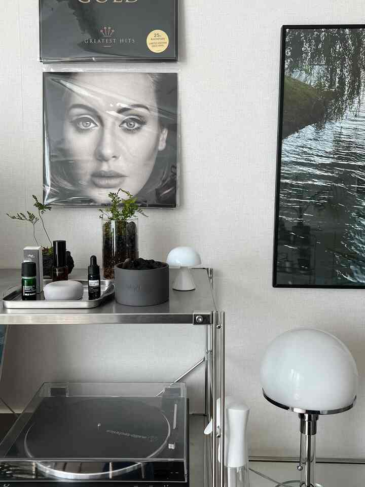 ベージュ色の壁を背景に金属製の棚とシンプルなインテリア小物が配置され、ディフューザーと照明が自然な雰囲気を演出する空間