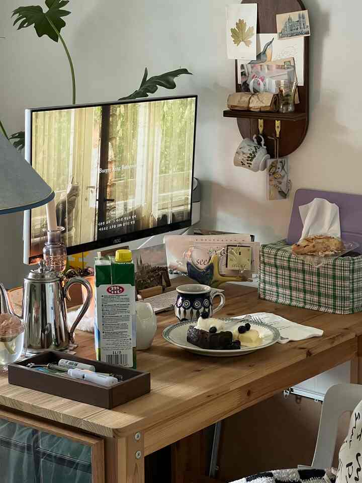 A cozy home cafe scene featuring a wood-toned desk with coffee, vintage tableware, and a computer monitor