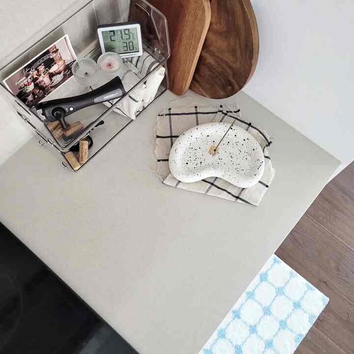 白とベージュのトーンのキッチンカウンター、木製まな板と透明な積み重ね収納棚、キャンドルが配置された雰囲気のある空間