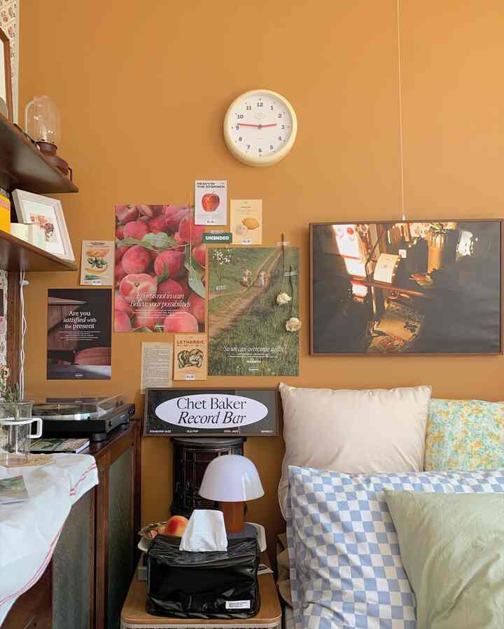 Living room with warm mustard walls featuring vintage audio equipment, wall clock, and various posters creating cozy ambiance