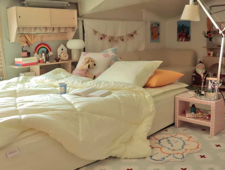 Natural yellow and beige-toned loft bedroom featuring a bed and sofa with baby dolls and children's decor for a warm, cozy atmosphere