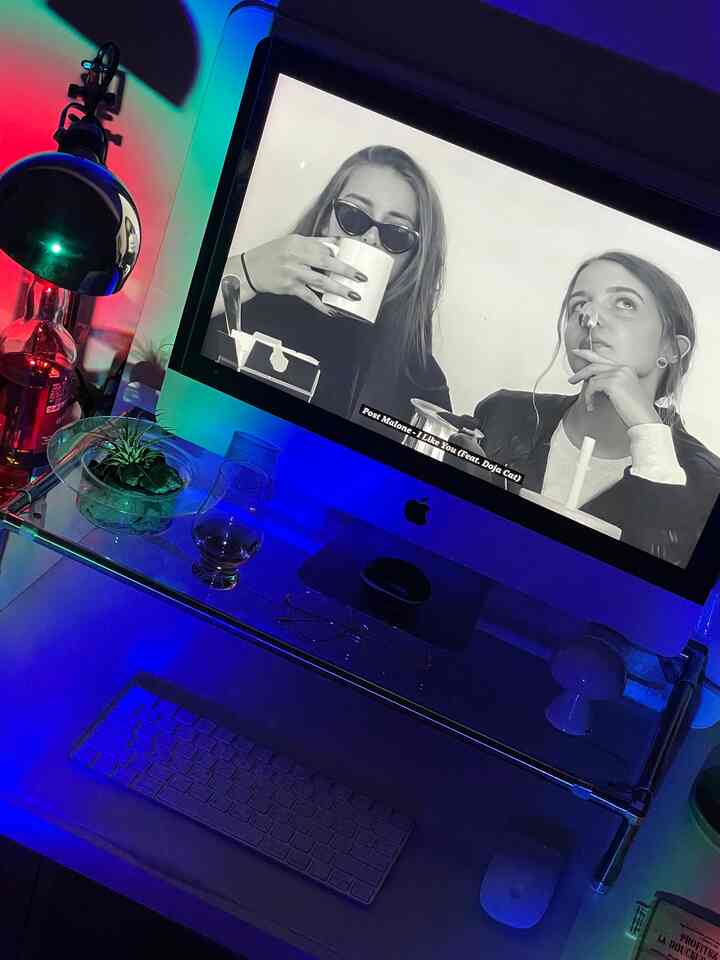 Modern home office with blue ambient lighting featuring an Apple computer on a stainless steel monitor stand and accessories