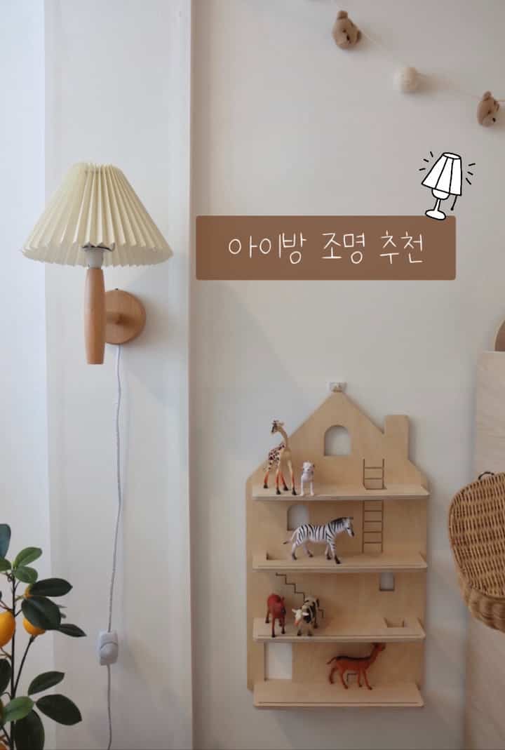 ナチュラルな木目調と白い背景の子供部屋、木製のおもちゃ棚と壁掛けライトが配された雰囲気のあるインテリア