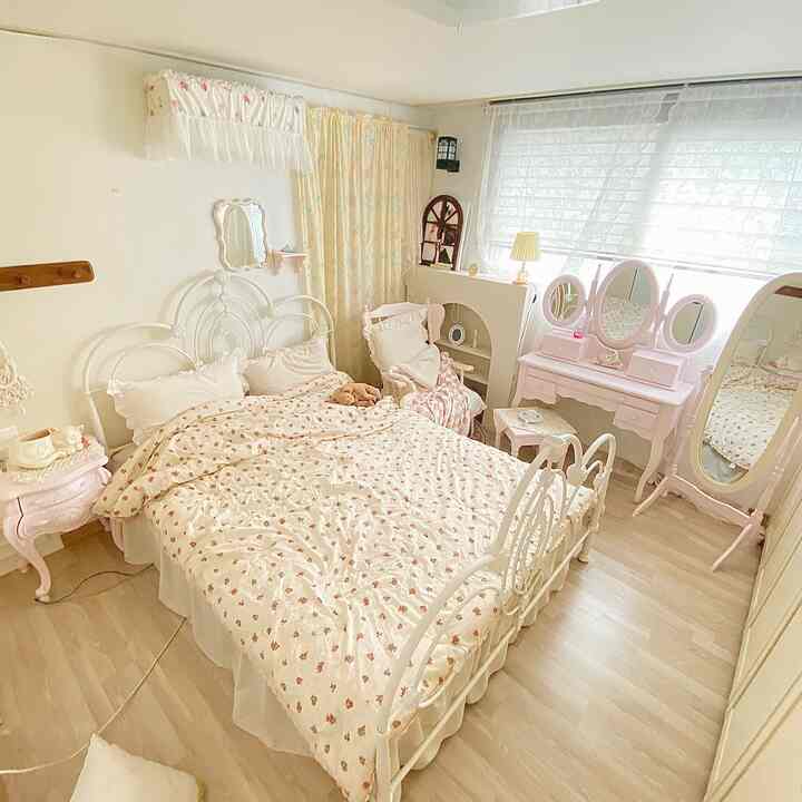 白とピンクのトーンが調和する寝室、アンティークベッドフレームとヴィンテージの化粧台が配置された雰囲気のあるインテリア