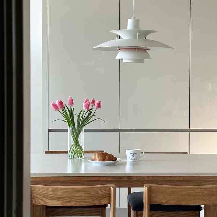 White and wood-toned kitchen featuring a central dining table with pink tulip vase and coffee mug, creating a cozy atmosphere