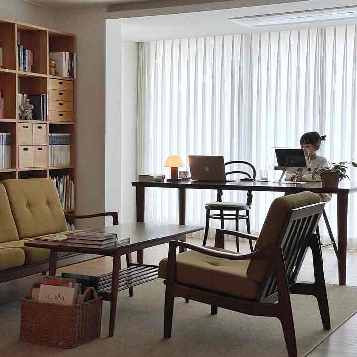 Natural wood tone living room study featuring yellow armchairs and a dining table where a child uses a laptop, creating a cozy atmosphere.
