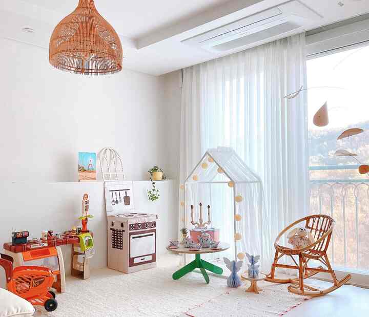 明るくナチュラルな色調の子供部屋、白いカーテンと木目調家具、赤ちゃんのおもちゃが配置された遊び空間