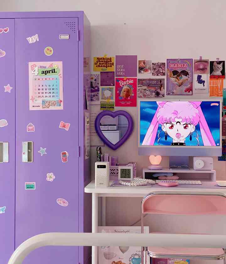 ピンクとパープルの色調のコンパクトな部屋、机とコンピューター、ポスターとハート型の鏡が配置された居心地の良いホームオフィス