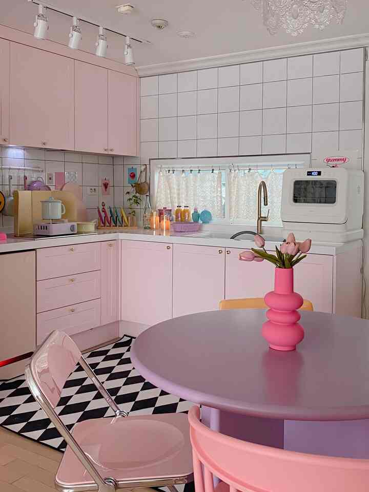 Cozy kitchen in pastel pink and lavender tones featuring pink cabinets, round table, and lace curtains with a modern look