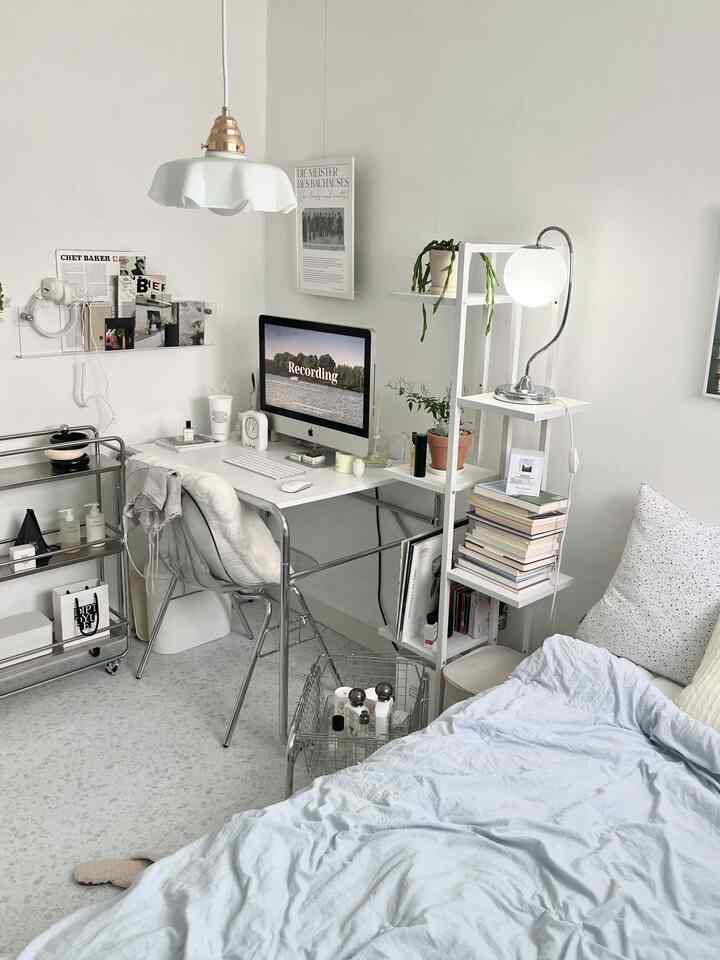 White and minimal tone bedroom with home office setup featuring desk, computer, storage cart, and bed in a neat interior