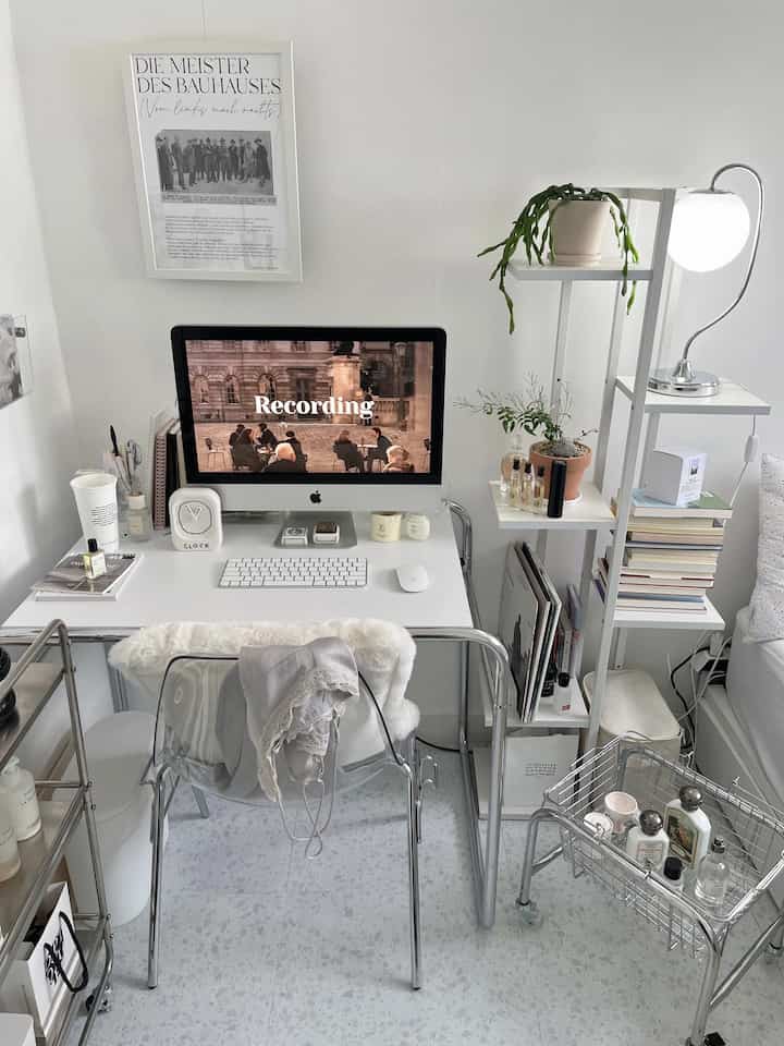 Minimal style home office in white and silver tones, featuring a desk with desktop computer and a shelf with plants, in a tidy small room