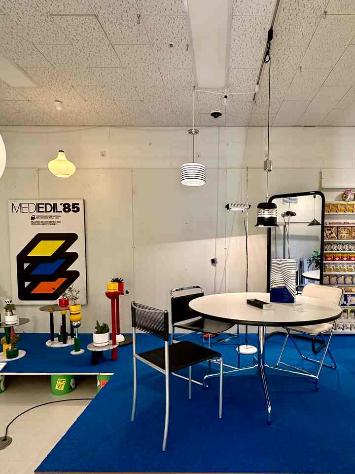 Modern dining space featuring a white wall and blue carpet with a round table and metal-framed chairs.