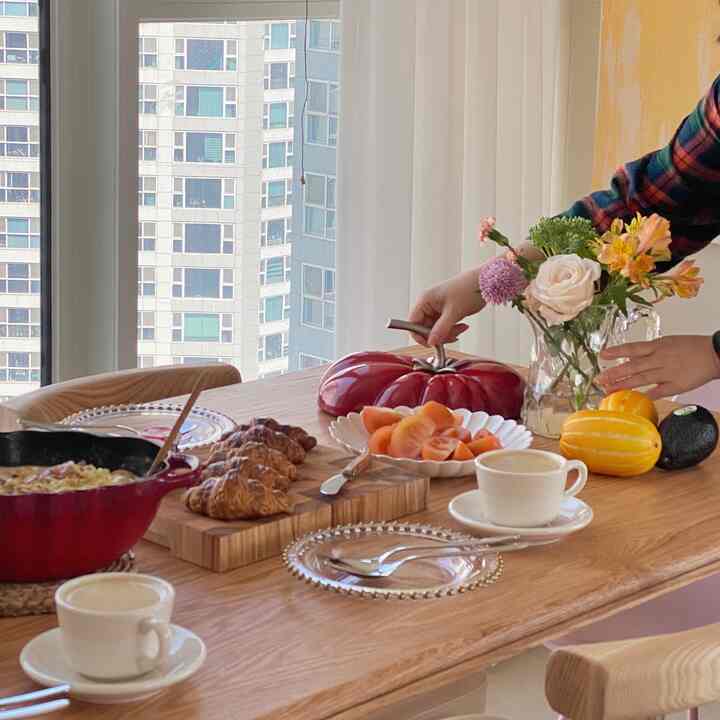 Bright white and natural wood-tone kitchen dining table featuring diverse plating and coffee cups for a home party and brunch