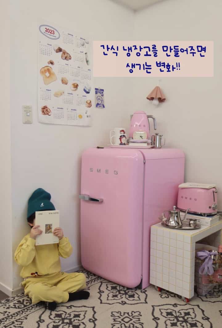 Bright pink SMEG refrigerator in living room with child sitting on patterned rug holding a book