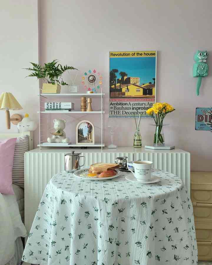 柔らかなピンクの壁と黄色い花が配置された居心地の良い寝室、白いテーブルにホームカフェセットが置かれている雰囲気のあるインテリア