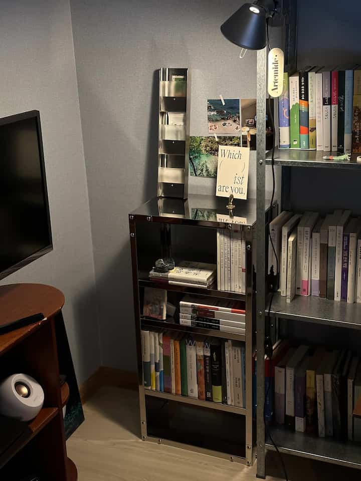 A study corner with gray walls and steel shelves complemented by natural wood flooring, featuring bookshelves and a desk in a cozy reading nook