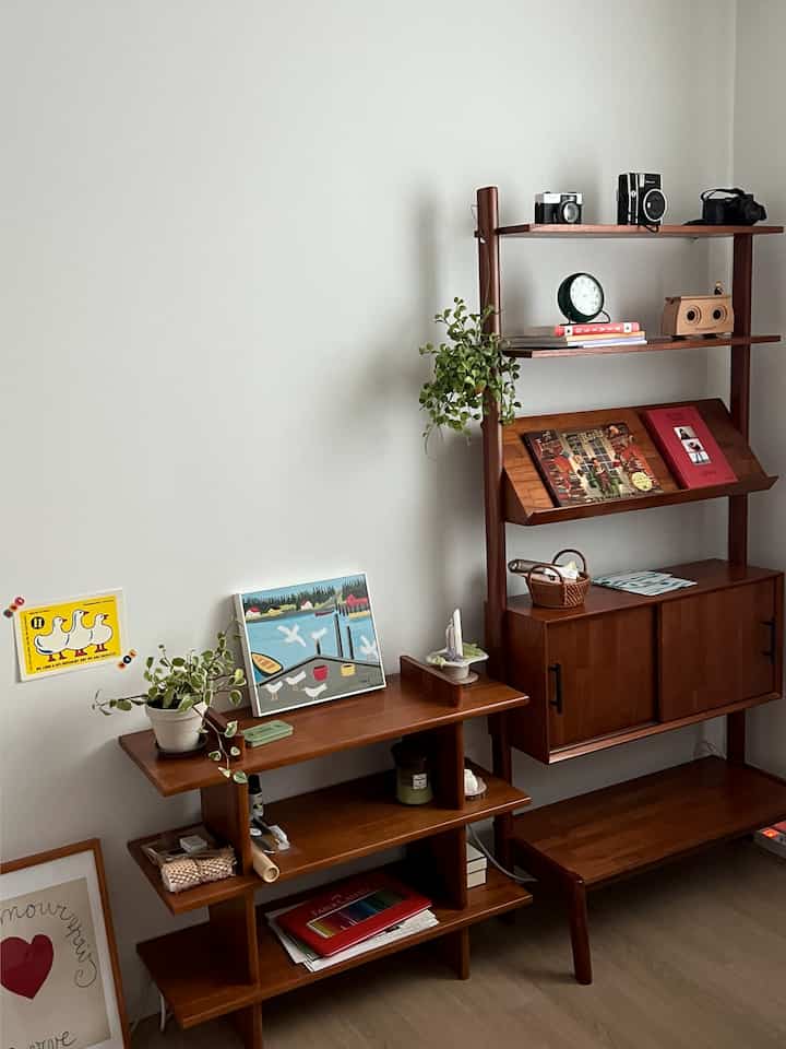 明るいホワイトの壁と木目調の棚やチェストが配置されたリビング、緑の植物や可愛らしい小物でアクセントをつけた雰囲気のあるインテリア