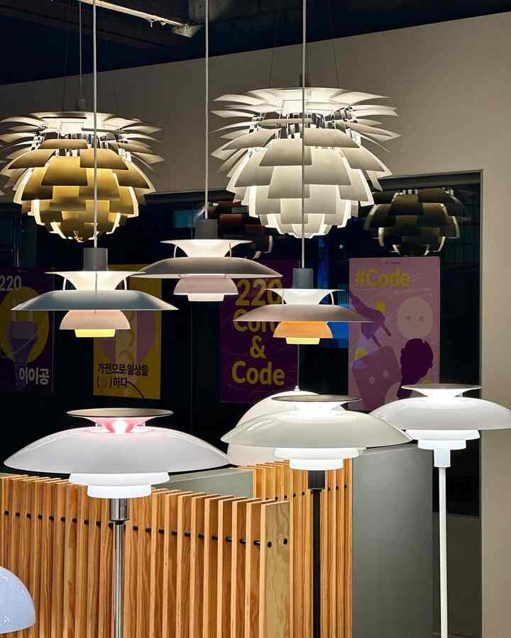 A modern showroom with white and wood tones featuring various Louis Poulsen pendant lights and floor lamps on display