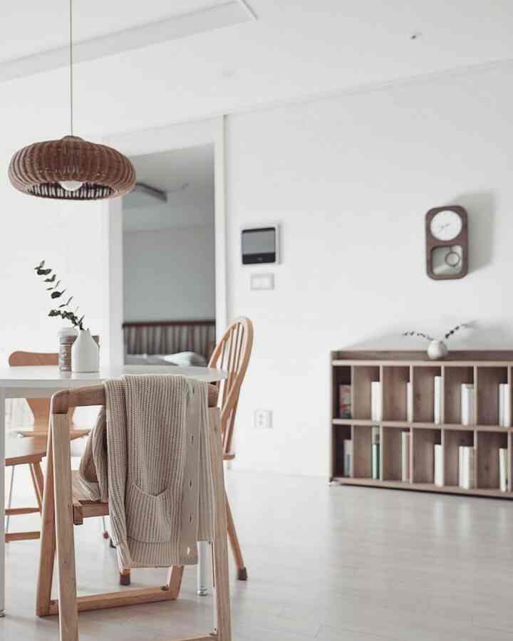 Natural wood tone dining chairs, wall clock and bookshelf arranged in a clean white dining room space