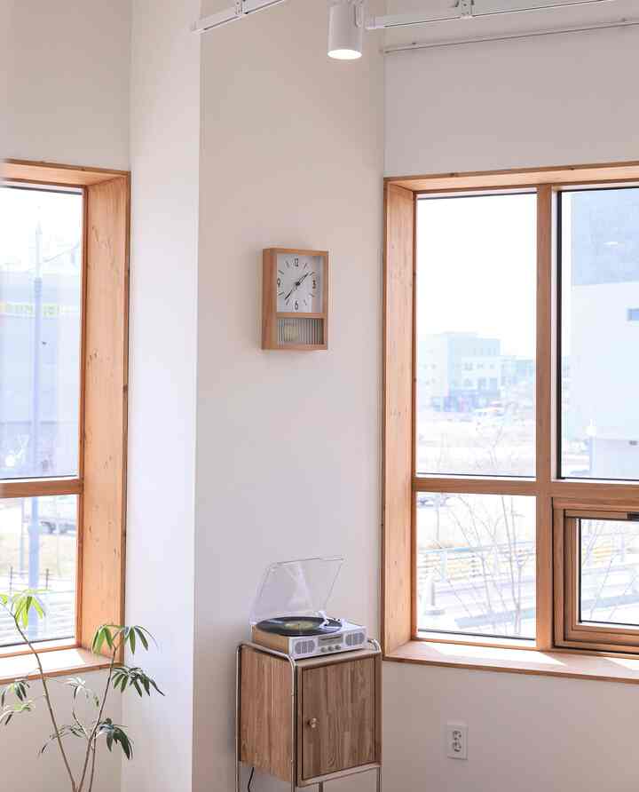 Natural-tone living room with bright cream walls, wooden window frames, featuring a wooden wall clock and LP player on a side table