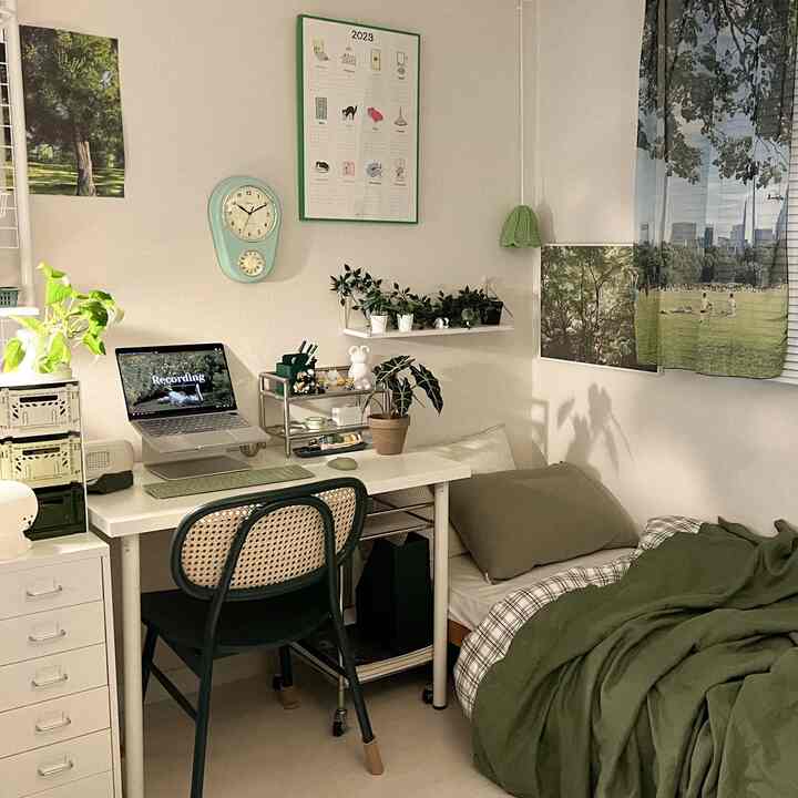 Green and white toned studio bedroom with desk and plants, featuring a simple and compact home office setup