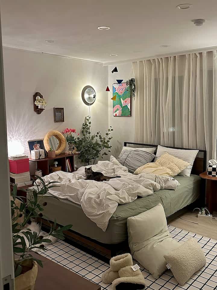 Natural toned bedroom featuring a central bed with a cat, shelves, and warm lighting creating a cozy atmosphere