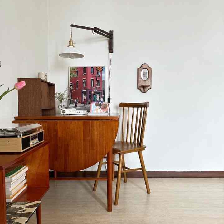 White walls and wood tone furniture create a Nordic-style study featuring a vintage record player and a wooden desk, evoking a cozy atmosphere