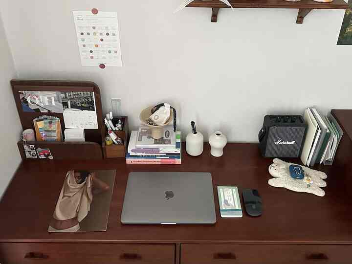 Dark brown wood-tone home office desk featuring laptop, books, and small decorative objets in a tidy setup