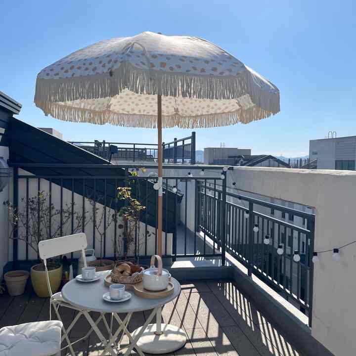Sky-blue terrace space featuring white outdoor furniture, vintage flower pots, and string lights creating cozy home cafe atmosphere