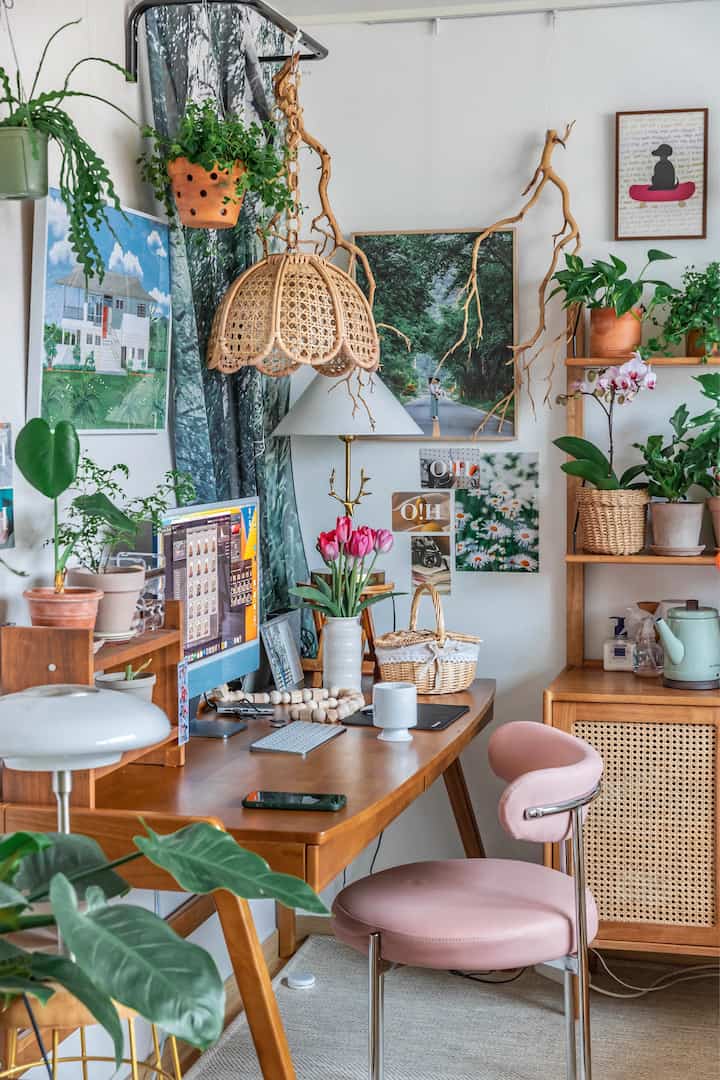 Natural wood tone study with green plants, pink chair, and rattan lighting creating a cozy workspace
