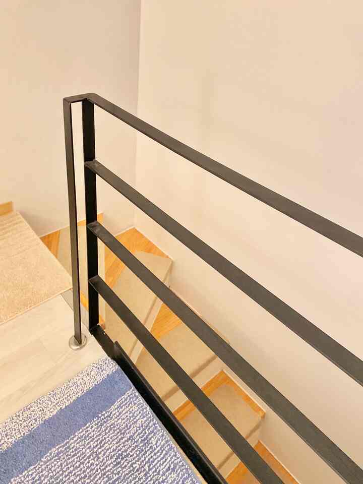 Natural wood-tone stairs and black water barrier railings in a cozy loft bedroom interior