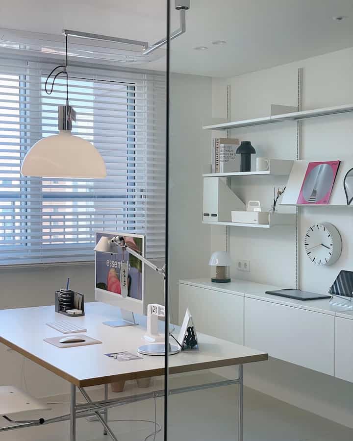 White-toned home office featuring a sleek desk with iMac, shelves, and minimal modern decor