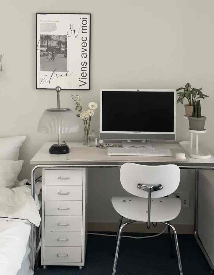 White and gray toned bedroom with home office setup featuring a computer desk and plants, showcasing a simple modern interior