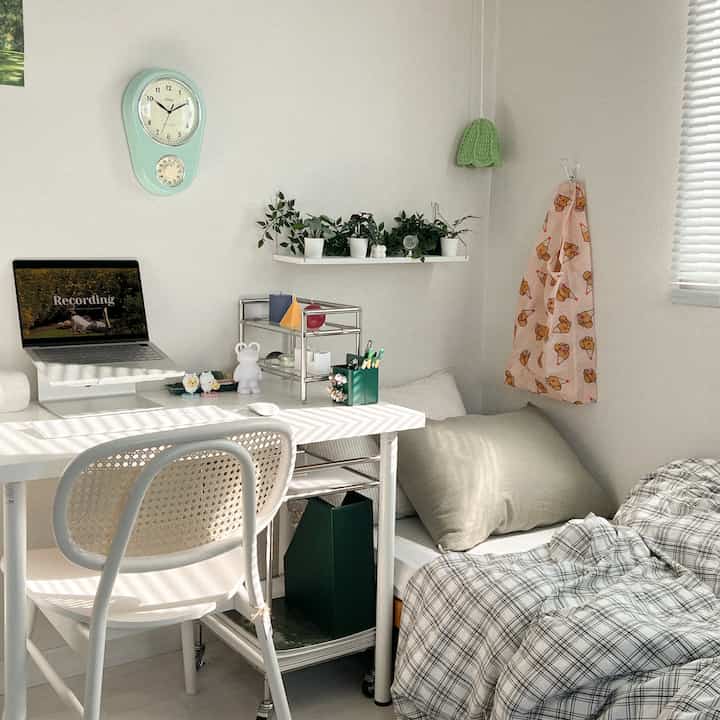 白と緑のトーンが特徴の小さい寝室兼ホームオフィス、デスクと植物が配置された印象的で清潔感のある空間